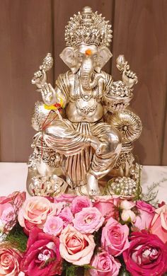 an elephant statue sitting on top of a table surrounded by pink flowers and greenery