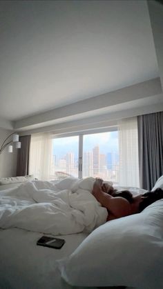 a woman is laying in bed with her head on the pillow and looking out the window