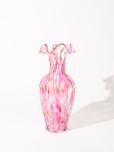 a pink and white glass vase sitting on top of a table next to a wall