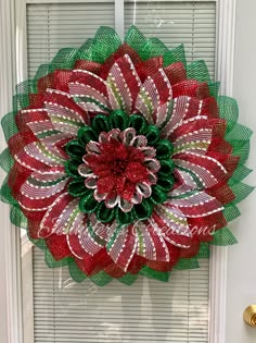 a red and green mesh wreath hanging on the front door with shutters behind it