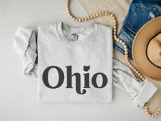 Show off your love for Ohio with our exclusive Ohio Imprint Gildan 18000 Crewneck Sweatshirt! Crafted with premium materials, this sweatshirt guarantees unbeatable comfort and durability. These garments are made from polyester and cotton. The collar is ribbed knit, so it retains its shape even after washing. There are no itchy side seams on these sweaters.  The classic crewneck design adds a touch of style to your outfit while keeping you warm during chilly days. Whether you're exploring the gre Ohio T Shirts, Ohio Sweatshirt, Ohio State Shirts, State Crewneck, Ohio Football, University Sweatshirts, Crewneck Design, Unisex Sweater, Unisex Gifts