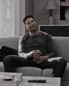 a man sitting on top of a couch next to a table with a remote control