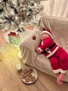 a baby is sleeping on a couch next to a christmas tree and some cookies in front of it