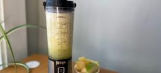 a blender sitting on top of a wooden table next to a bowl of fruit