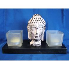 a white buddha statue sitting on top of a table next to two glass cups and a candle holder