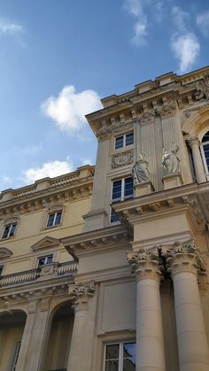 an old building with columns and a clock on the front, against a cloudy blue sky