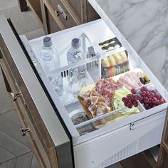 an open refrigerator filled with lots of food on top of a marble floored kitchen counter