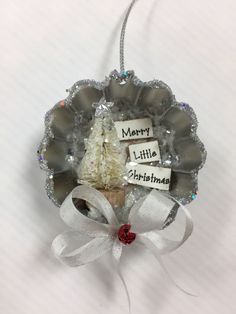 a christmas ornament hanging on a wall with a white ribbon and silver ornaments