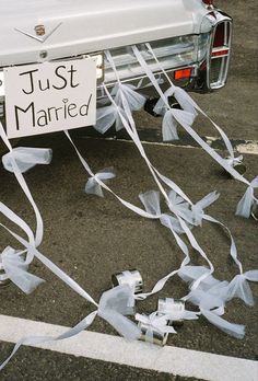 a white car parked next to a sign that says just married with streamers in front of it