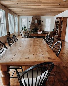 a large wooden dining table surrounded by black chairs in a room with white walls and wood flooring