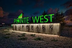 a sign that reads point west autopark at night in front of some bushes and trees