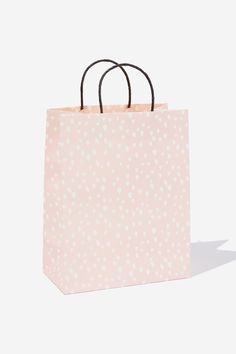 a pink shopping bag with white polka dots on the front and black handles, against a white background