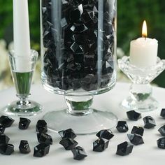 a glass vase filled with black rocks next to a candle and some candlesticks