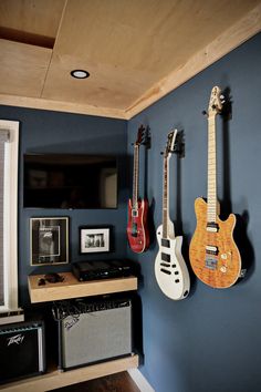 three guitars are hanging on the wall next to an amp and guitar amplifier in a room with blue walls