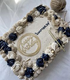 a birthday cake decorated with blue flowers and gold decorations on a table next to balls of yarn