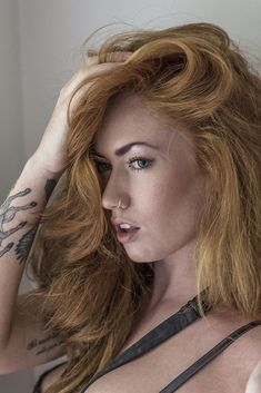 a woman with red hair and tattoos on her chest posing for the camera, holding her hand to her head