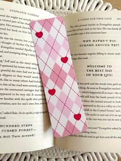 an open book with a pink and white checkered tie laying on top of it