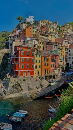 boats are parked on the water in front of colorful buildings and cliffs, along with green grass