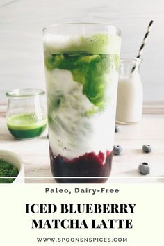 a glass filled with green and red liquid next to a bowl full of blueberries