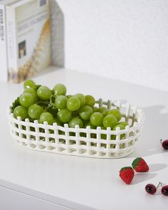 some grapes in a white basket on a table next to cherries and a book