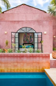 a pink house with a pool in the foreground and potted plants on the other side