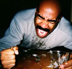 a man with his mouth wide open holding a shot glass in front of him and looking at the camera