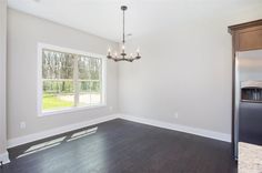 an empty living room with hard wood flooring and a chandelier hanging from the ceiling