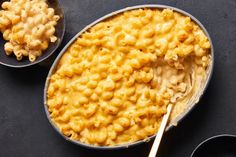 macaroni and cheese is in two bowls with spoons next to it on a black surface