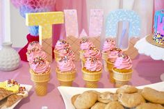 a table topped with ice cream cones filled with pink frosting and sprinkles