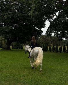 a woman riding on the back of a white horse across a lush green field next to trees