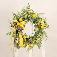 a yellow wreath with lemons and greenery on a white ladder against a wall