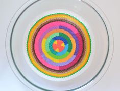 a glass bowl filled with colorful crochet coasters on top of a white table