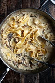 a pot filled with pasta and mushrooms on top of a wooden table