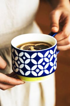 a woman is holding a cup of coffee in her left hand and the other one has a spoon in it