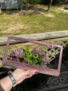 a person holding up a pink glittered mirror with flowers in the backgroung