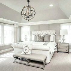 a large white bed sitting under a chandelier in a bedroom next to two windows