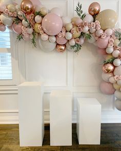 balloons and flowers are arranged on the wall in front of two white pedestals, one with