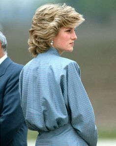 the woman is wearing a blue suit and standing in front of another man with his hand on his hip