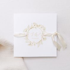 a white card with gold foiling and a ribbon tied around the front of it