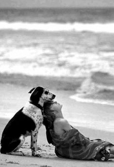 a woman laying on top of a beach next to a dog