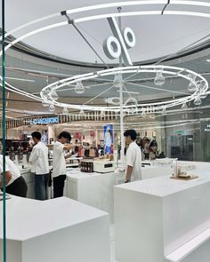 people are standing in the middle of a store with white counters and round lights hanging from the ceiling