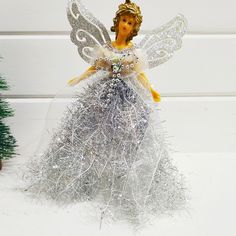 a tinsel angel figurine next to a small christmas tree on a white surface