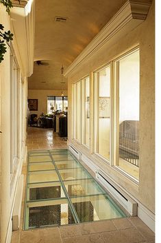 a long hallway with glass flooring and windows on both sides, leading to a balcony