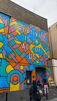 people walking in front of a colorful building with words painted on the side and below it