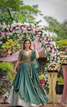 a woman standing in front of a floral arch wearing a green dress and gold jewelry