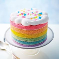 a rainbow cake with white frosting and sprinkles on top sits on a plate