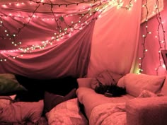 there is a bed with pink sheets and lights on the wall above it, next to a laptop computer