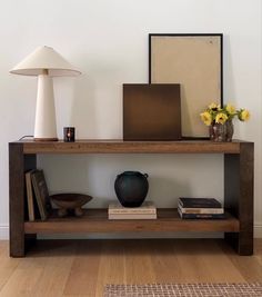 a wooden shelf with books and vases on it in front of a white wall