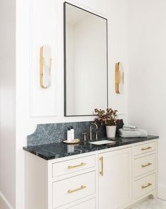 a white bathroom with marble counter tops and gold pulls on the mirror above the sink