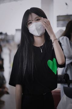 a woman wearing a face mask with a green heart on the front, and a black t - shirt behind her